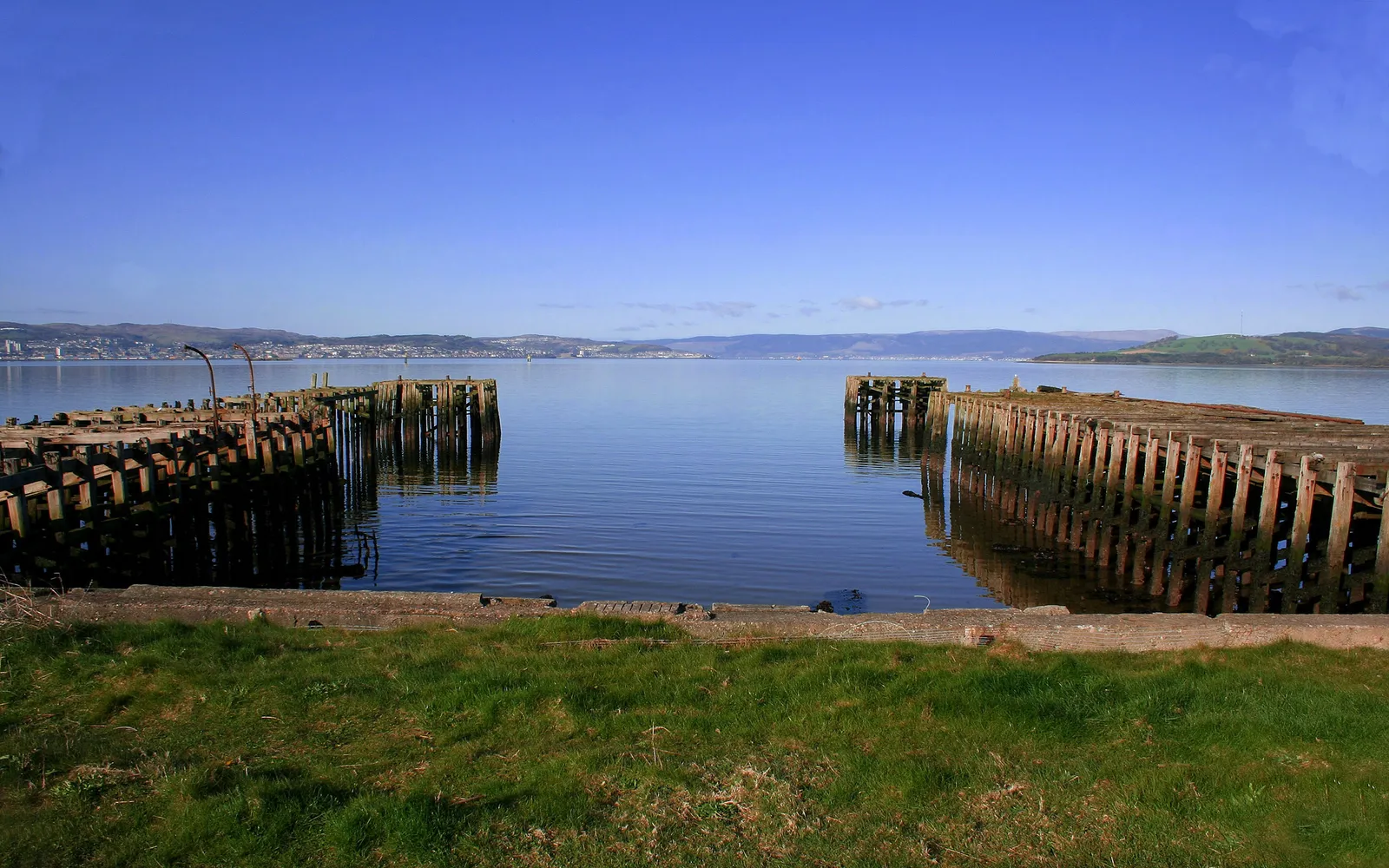 Two old wooden piers jut out into a calm body of water under a clear blue sky.