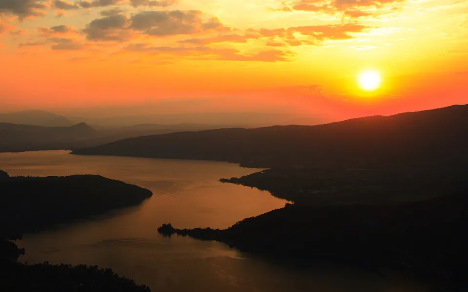 Orange sunset light reflects on a calm mountain lake with silhouetted mountains.
