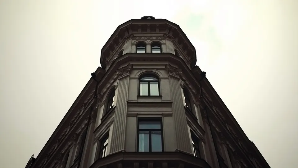 A low-angle view of a detailed, multi-story building with arched windows against a bright, overcast sky.