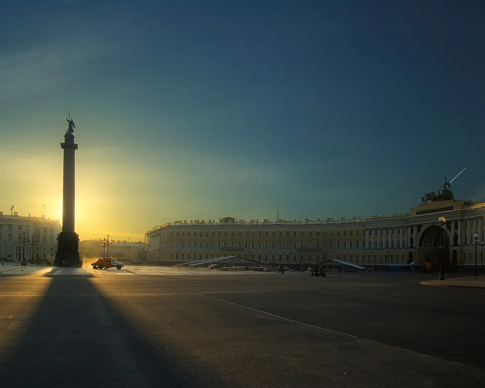 A wide shot of Palace Square in St. Petersburg at sunrise, with the Alexander Column casting a long shadow.