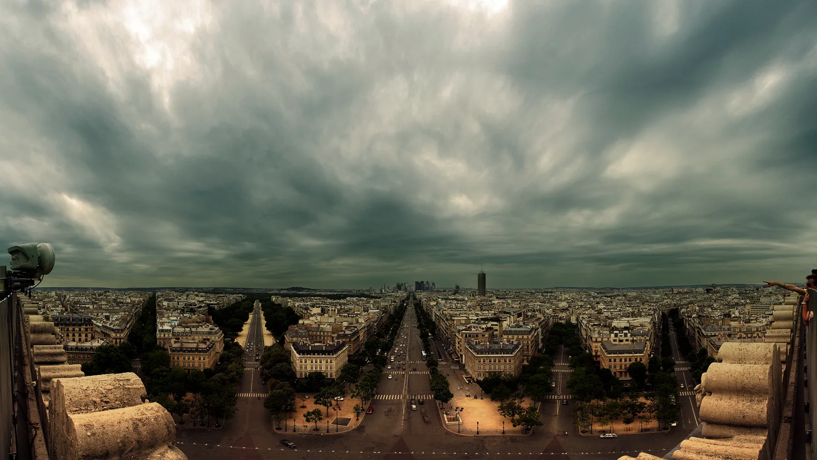 A wide panoramic view of the city of Paris with a dramatic cloudy sky overhead.