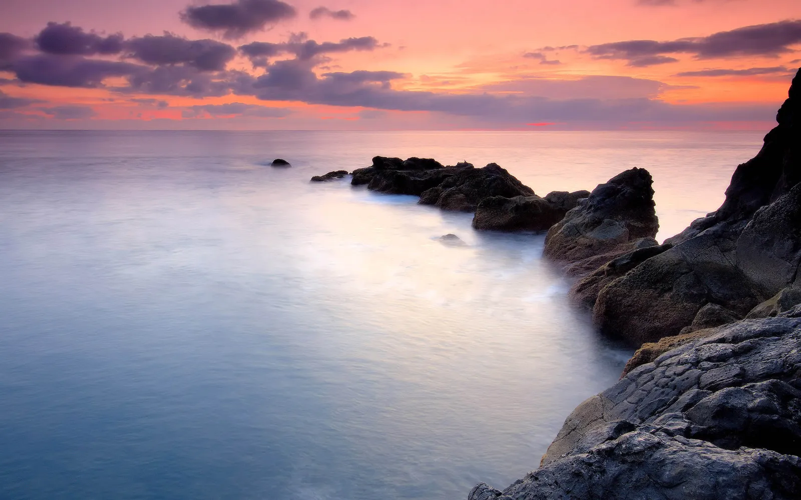 A serene coastal scene at sunset with pastel colors in the sky and calm water.