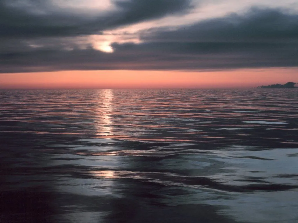 A peachy sunset glow reflects on the gentle waves of the ocean.