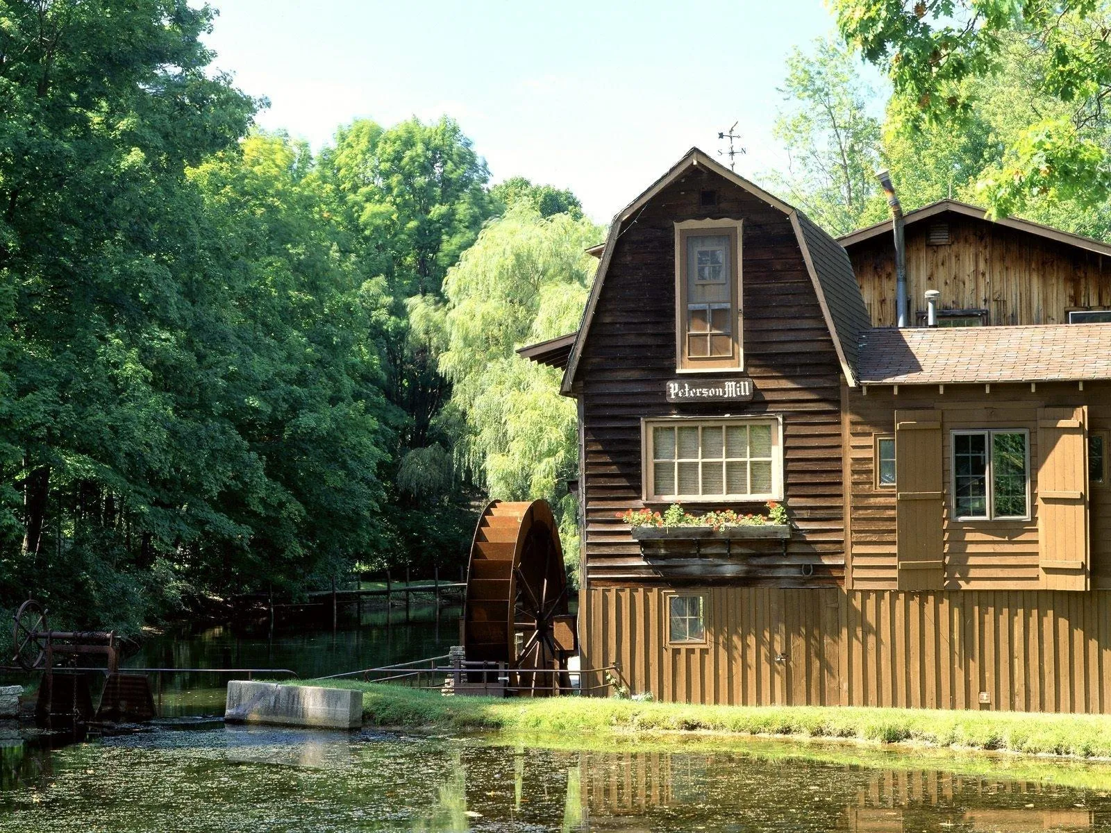 A historic wooden mill building with a large water wheel beside a reflective pond.