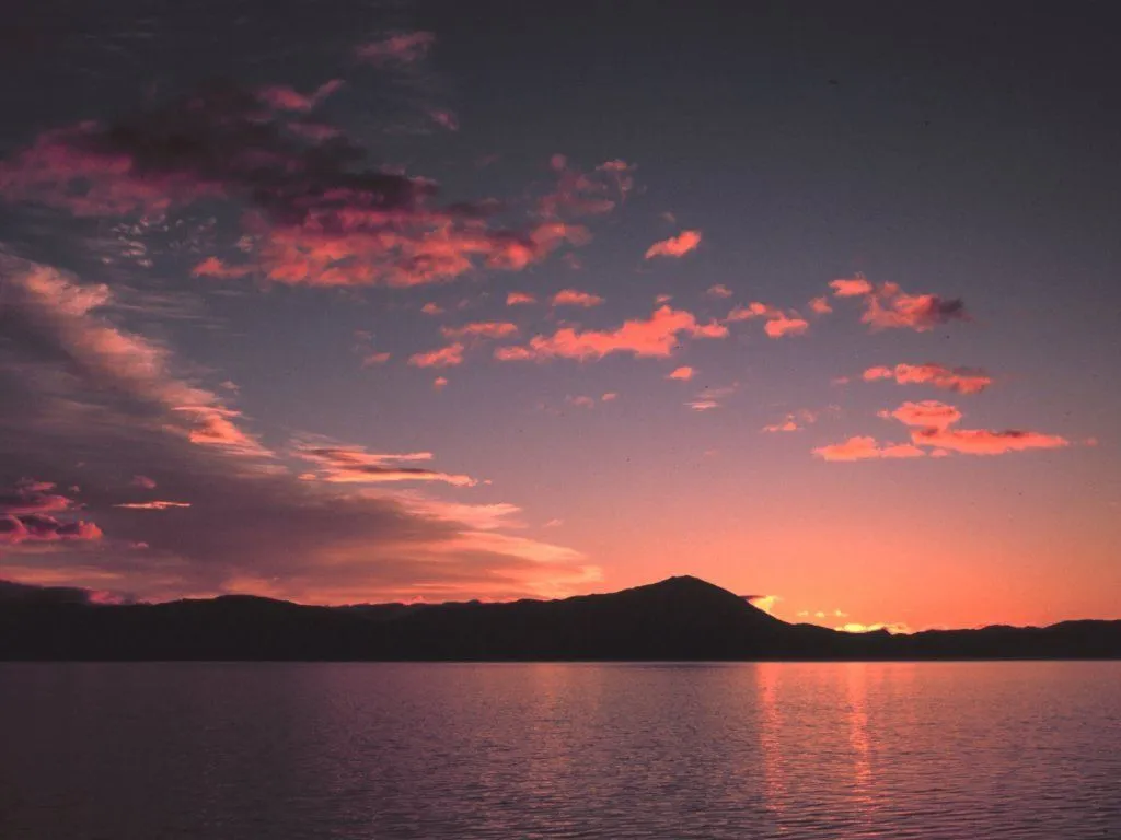Pink and orange clouds streak across the sky at sunset, reflected in a calm lake.