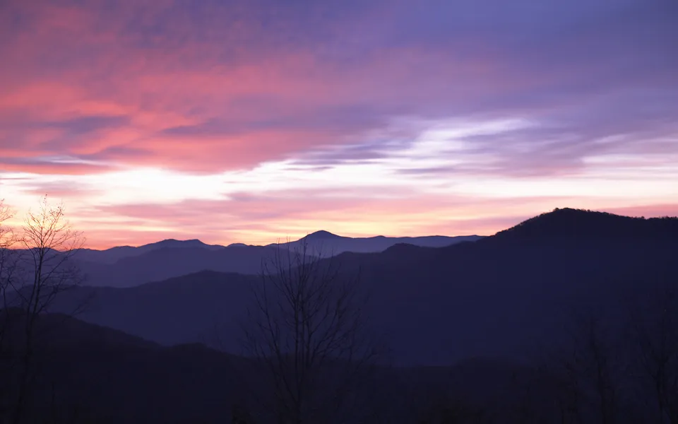 A vibrant sunrise with pink and purple hues paints the sky over silhouetted mountain ranges.