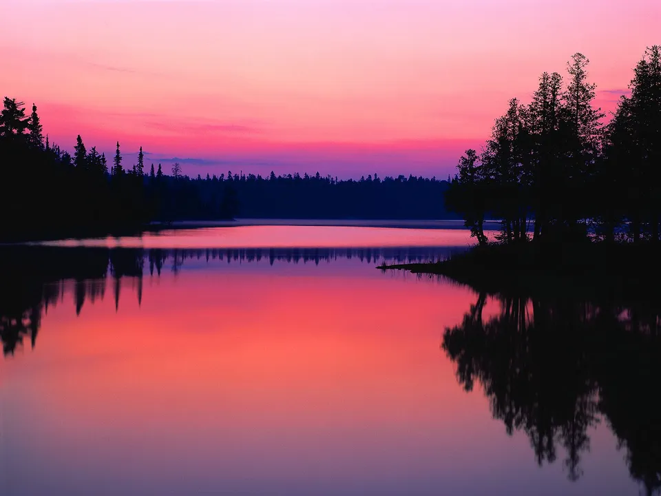 A serene sunset with soft pink and purple hues perfectly mirrored on the calm lake surface.