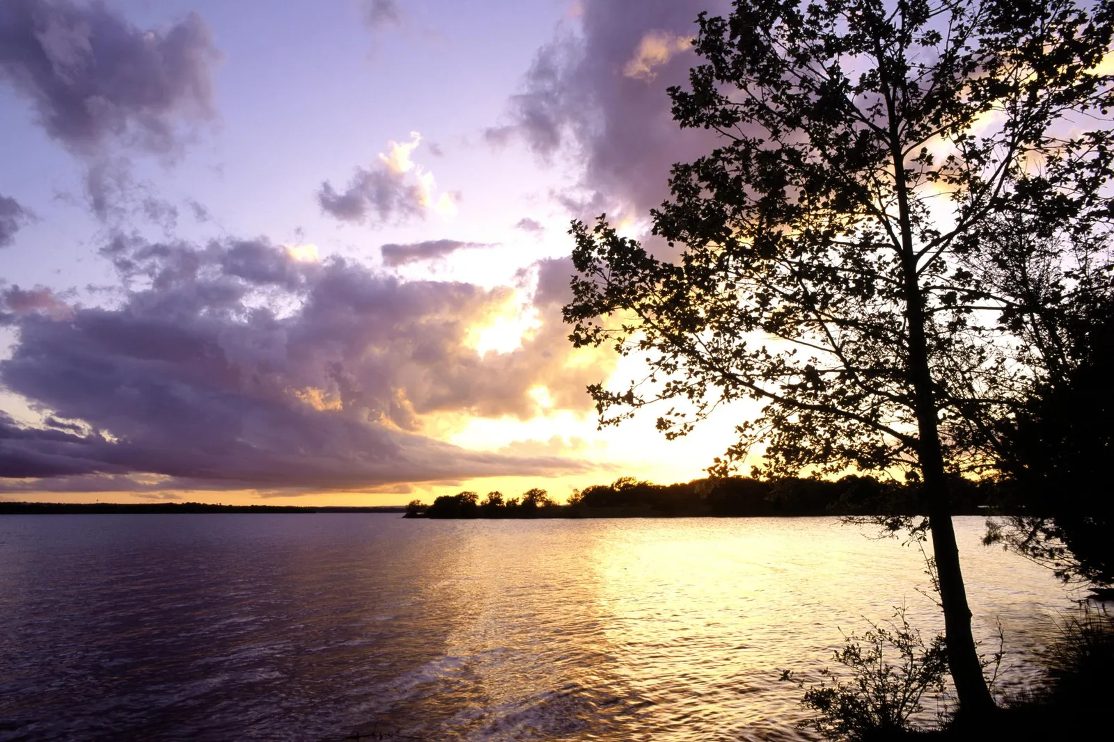 A tranquil lake reflects the purple and gold hues of a sunset sky.