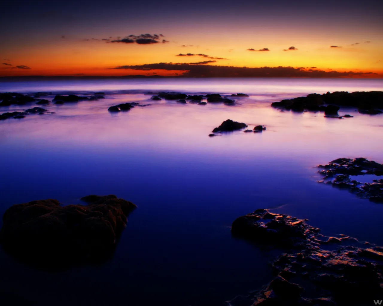 A sunset with purple hues over a rocky ocean coastline.