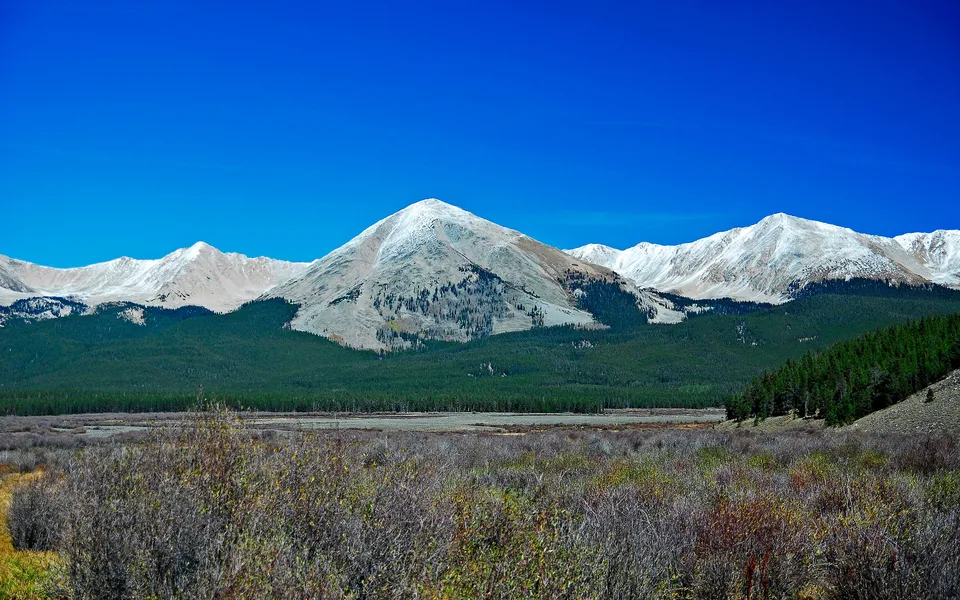 A prominent pyramid-shaped mountain peak is lightly dusted with snow, set against a deep blue sky.