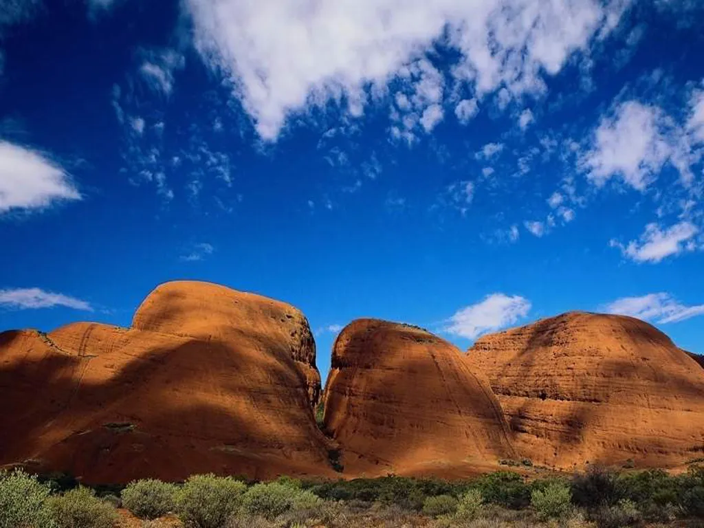 Large, rounded red rock formations dominate the landscape under a bright blue sky with scattered white clouds.