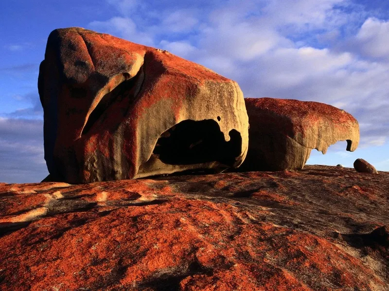 Large, weathered granite boulders with red lichen and blue sky with clouds.