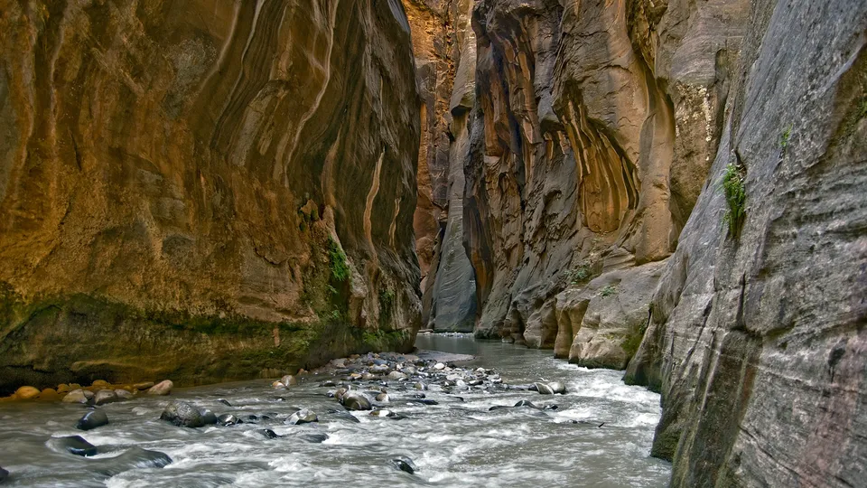 A river flows through a narrow canyon with towering, textured rock walls.