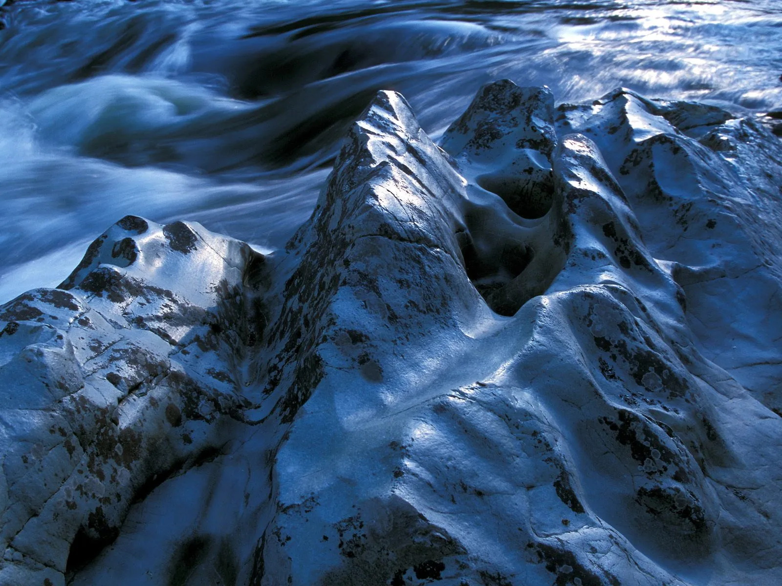 Close-up of smooth, sculpted river rocks with flowing water in the background.