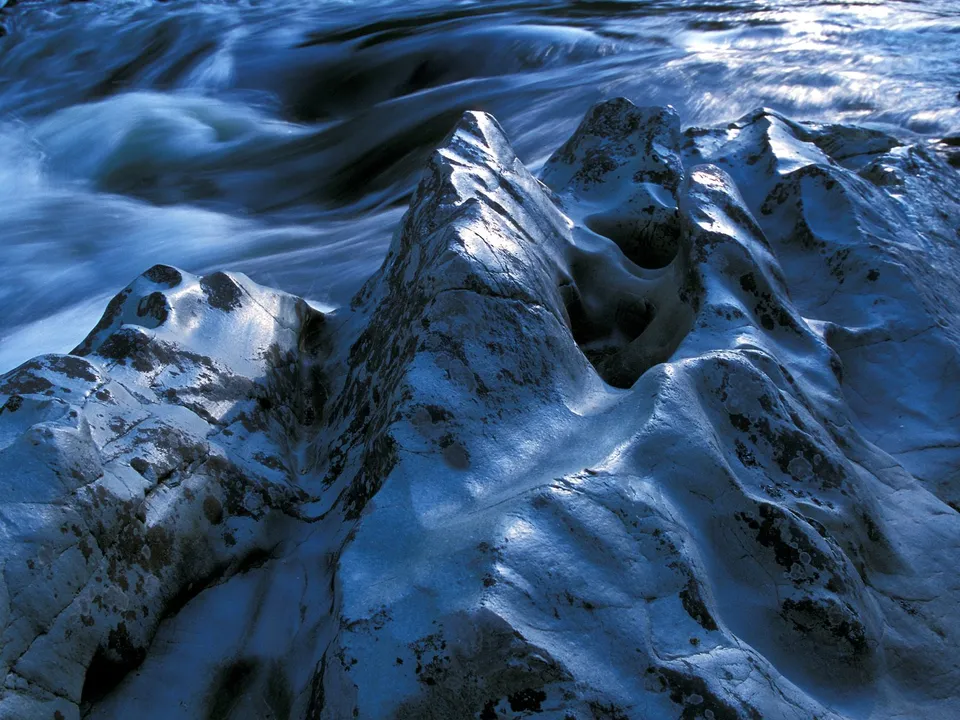 Close-up of smooth, sculpted river rocks with flowing water in the background.