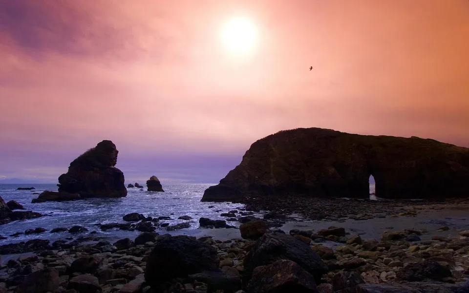 A rocky coastline with sea stacks and an archway under a vibrant pink and orange sunset sky.
