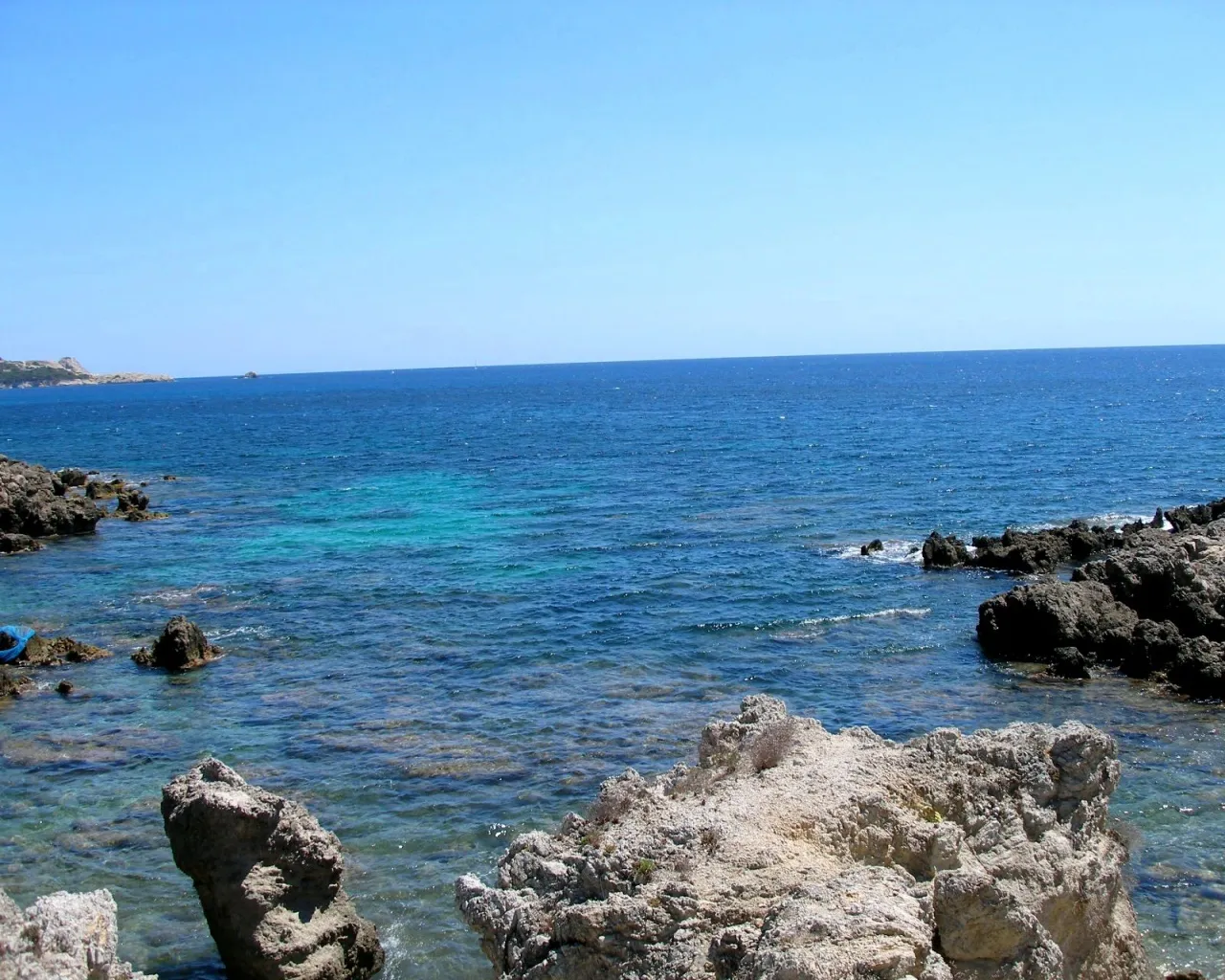 A clear blue sky above a rocky coastline with turquoise water lapping at the shore.