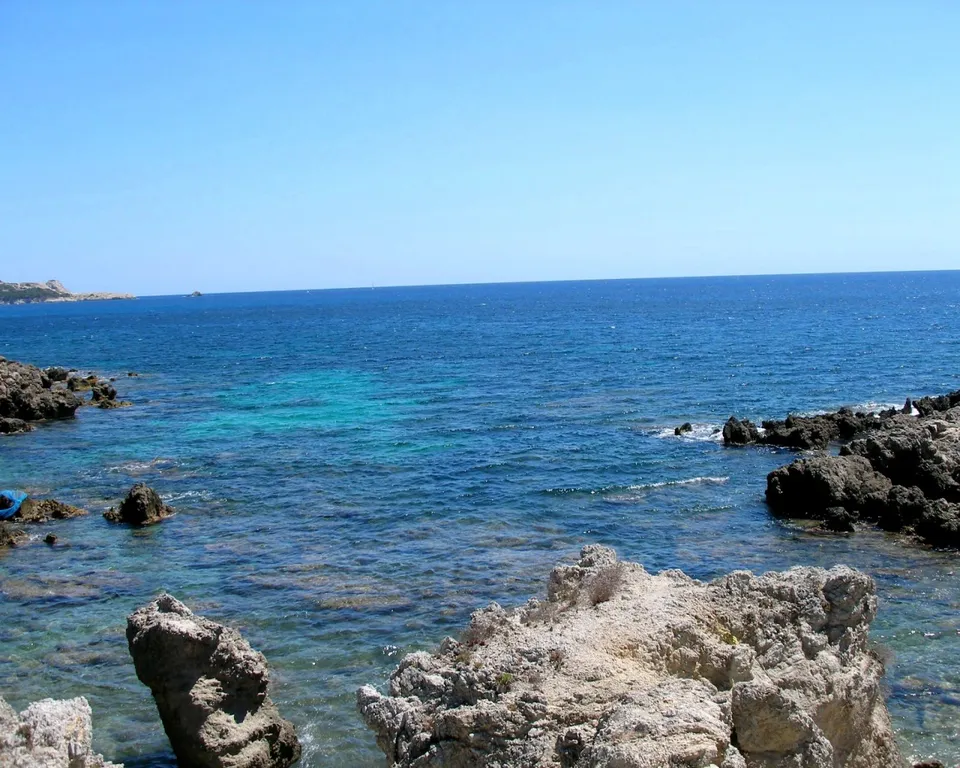 A clear blue sky above a rocky coastline with turquoise water lapping at the shore.
