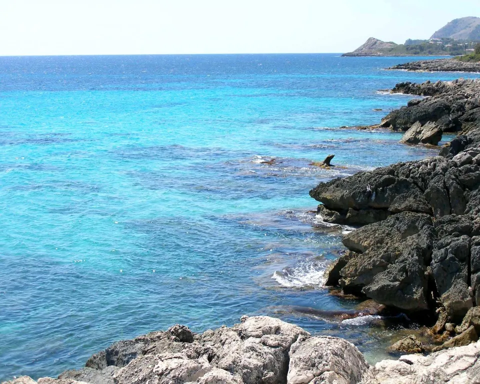 A rocky coastline with clear turquoise water lapping against dark gray rocks.