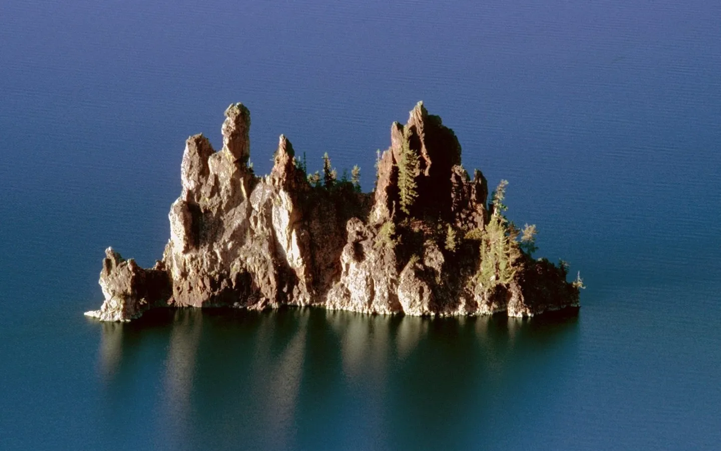 A rugged, rocky island with sparse trees rises from a vast expanse of deep blue water.