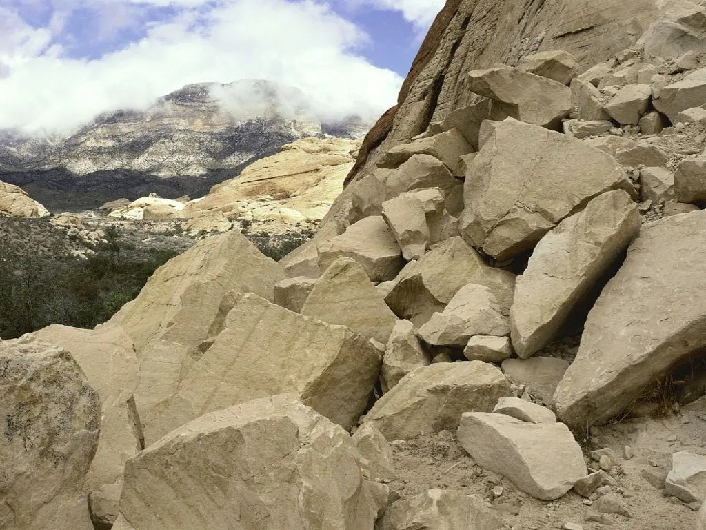 A pile of large, light-colored rocks in the foreground with mountains and clouds in the background.