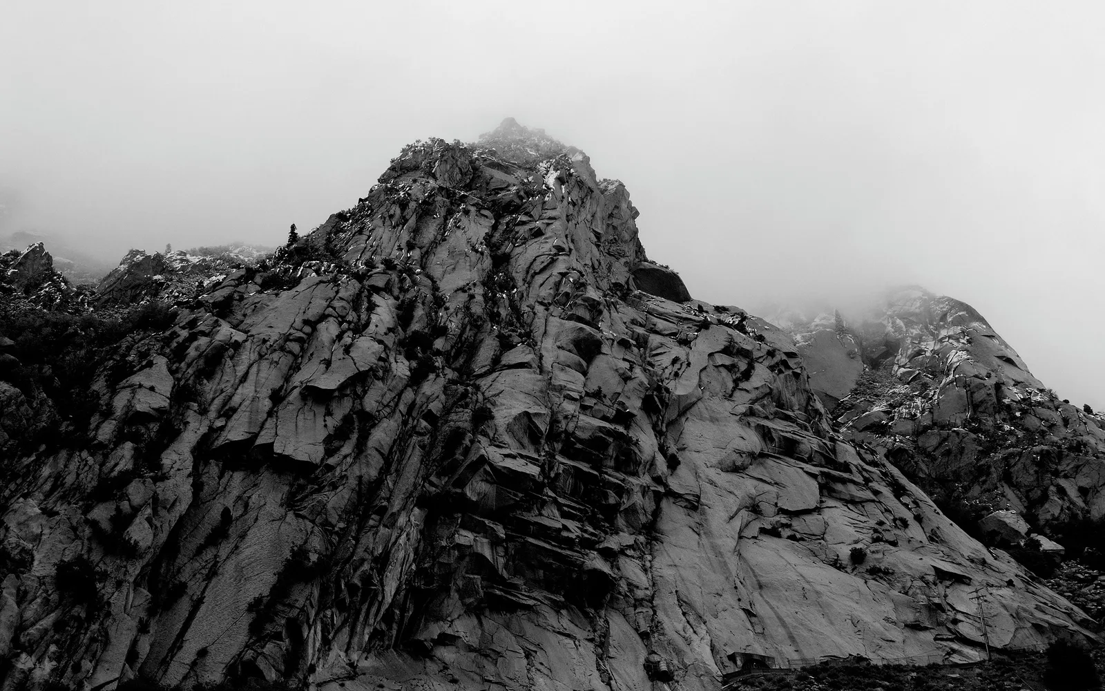 A dramatic, low-angle view of a rugged, rocky mountain peak partially obscured by swirling mist and clouds.