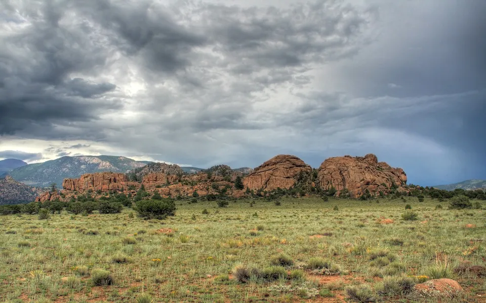 A wide landscape view of large, rounded rock formations in the foreground under a dramatic, cloudy sky.
