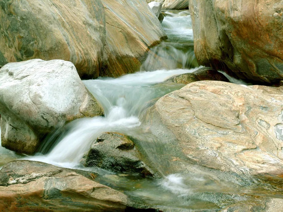 A close-up view of a river flowing over smooth, textured rocks with silky water.