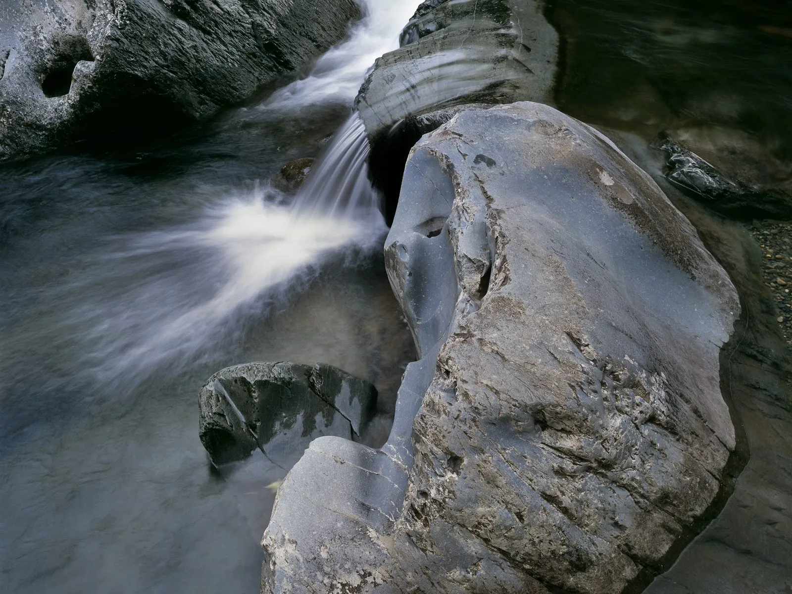 A close-up view of a river with smooth, blurred water flowing over dark, textured rocks.