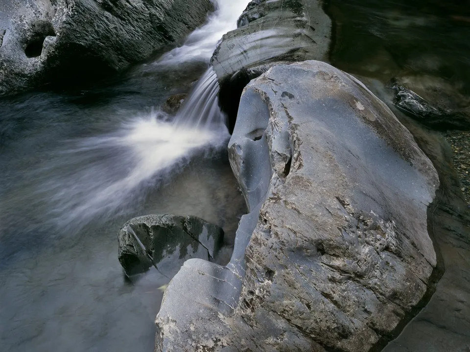 A close-up view of a river with smooth, blurred water flowing over dark, textured rocks.