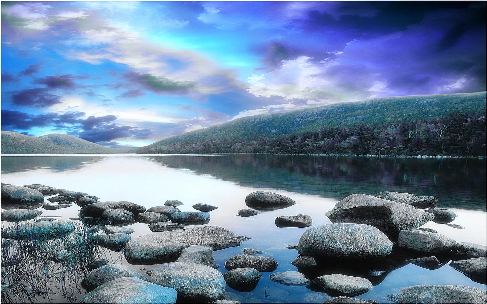 A serene lake with smooth rocks in the foreground reflecting a dramatic cloudy sky with purple and blue hues.