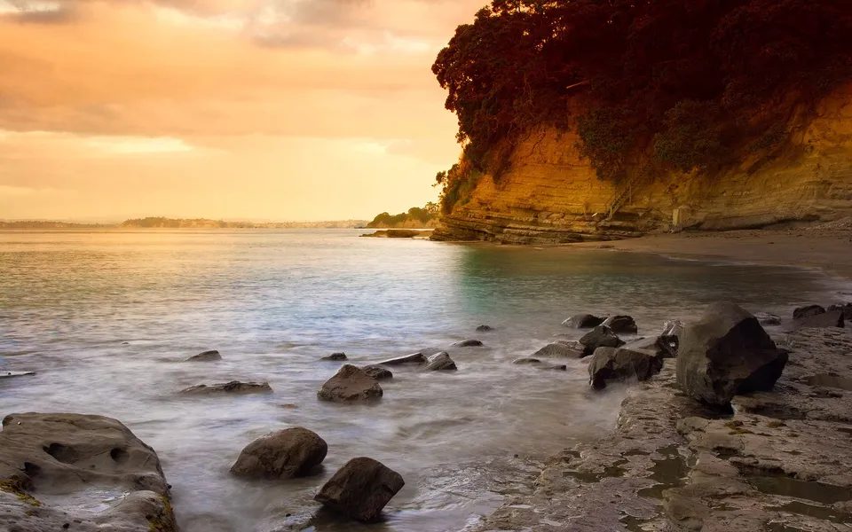 A rocky shoreline with calm water and a golden sky at sunset.