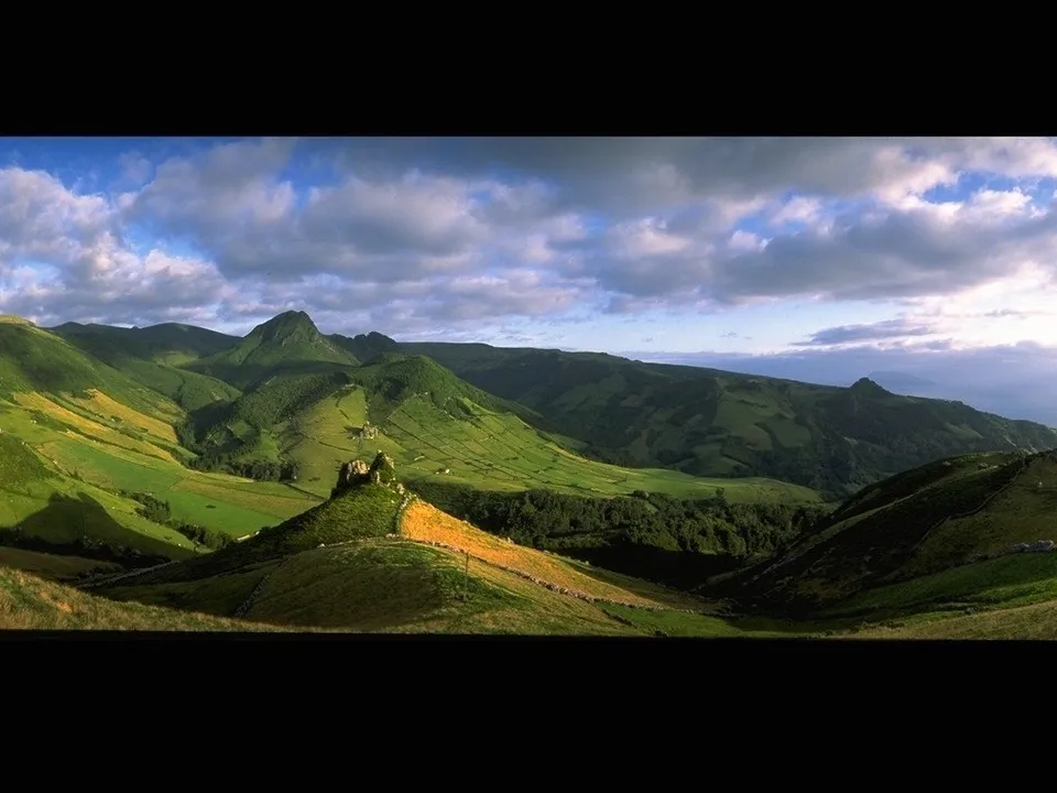 Vast green rolling hills with a dramatic cloudy sky above.