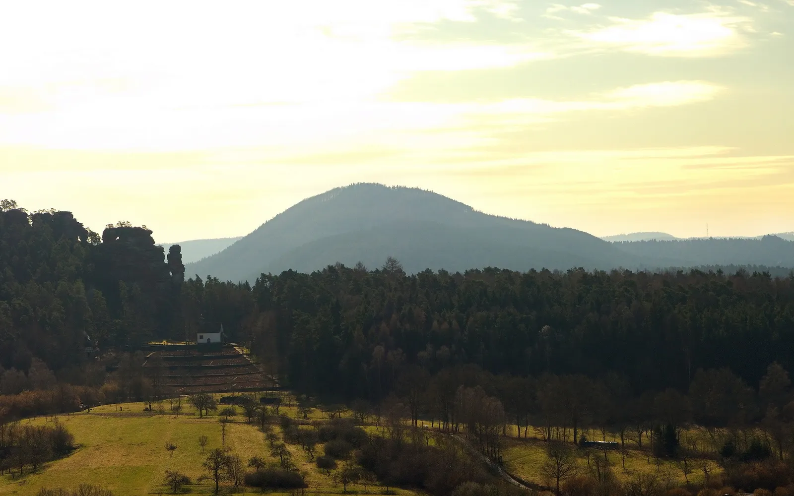 A wide view of rolling hills covered in trees, with a small white building on a terraced slope.