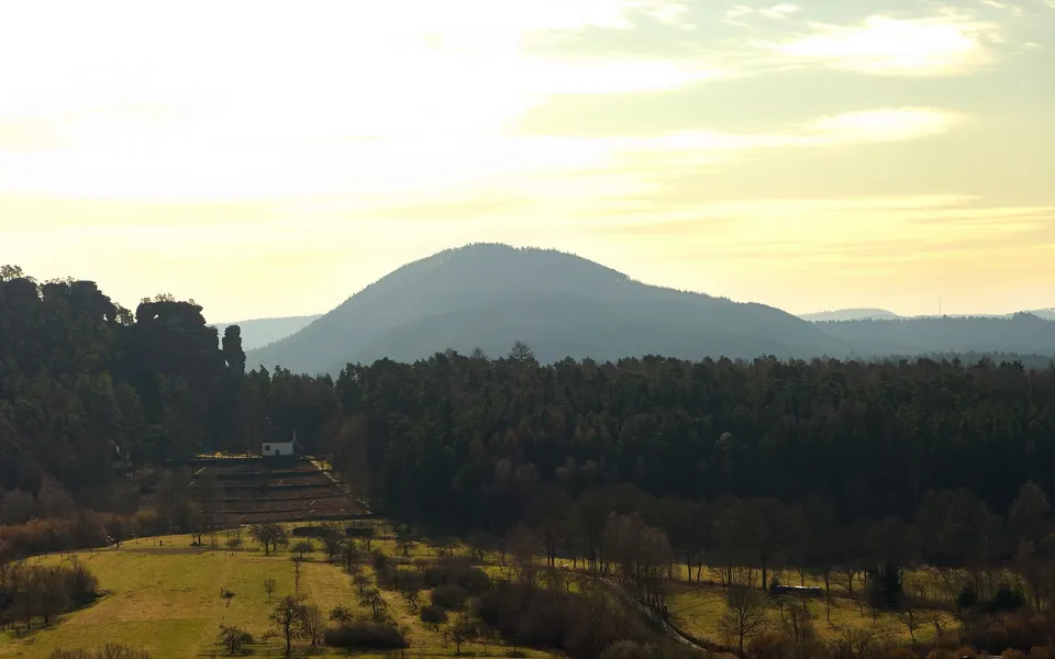 A wide view of rolling hills covered in trees, with a small white building on a terraced slope.
