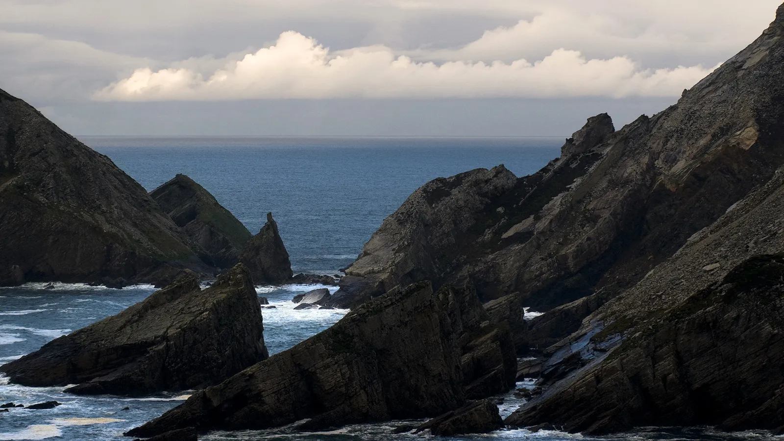 Jagged, dark rock formations rise from the sea under a cloudy sky.