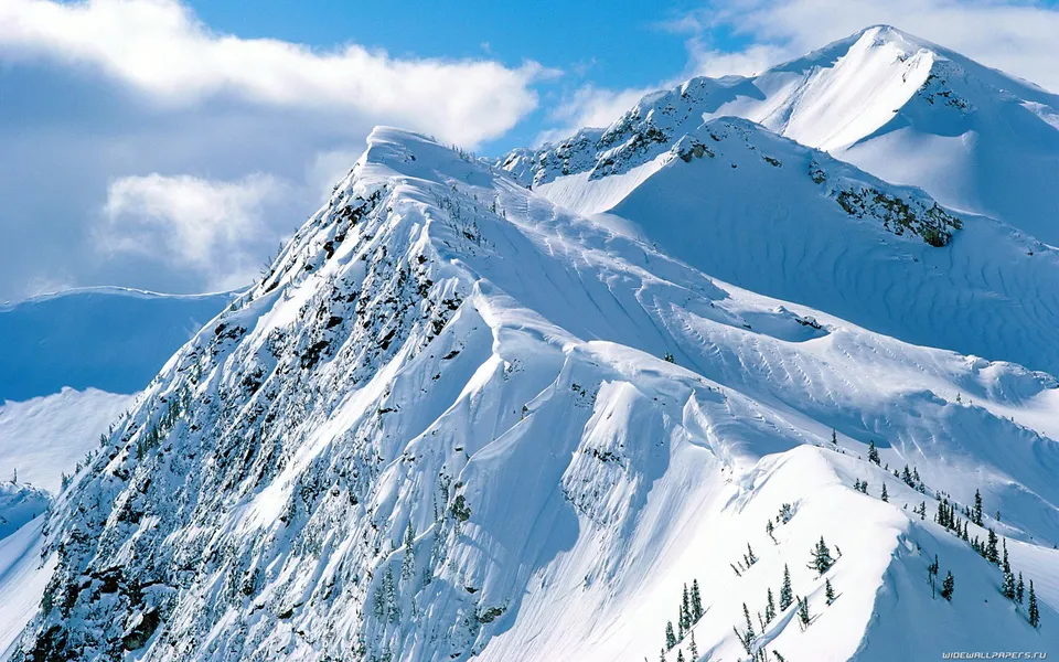 Dramatic snow-covered mountain peaks with sharp ridges and deep valleys, highlighted by sunlight and shadows.