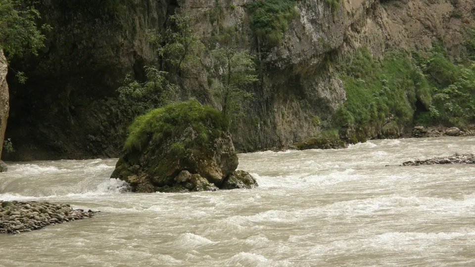 A wide, fast-flowing river with white water rushes through a rocky gorge with steep, vegetated cliffs.
