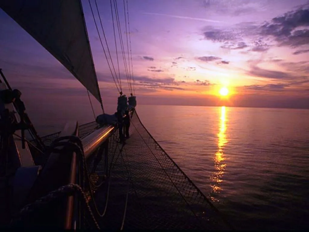 View from a sailboat deck looking towards the ocean as the sun sets.