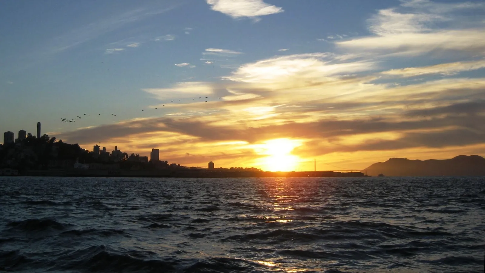 A vibrant sunset over the water with the San Francisco skyline silhouetted against the colorful sky.