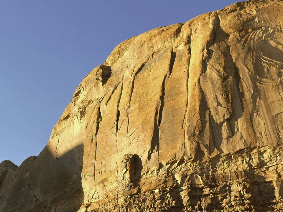 A close-up view of towering golden sandstone cliffs against a clear blue sky.