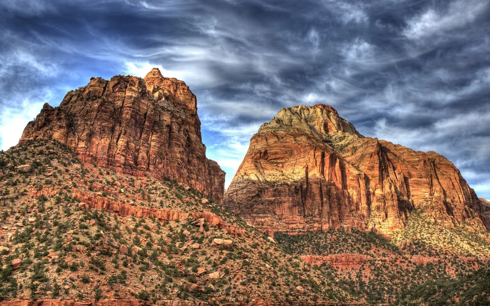 Two massive sandstone mountains rise under a dramatic sky with swirling clouds.
