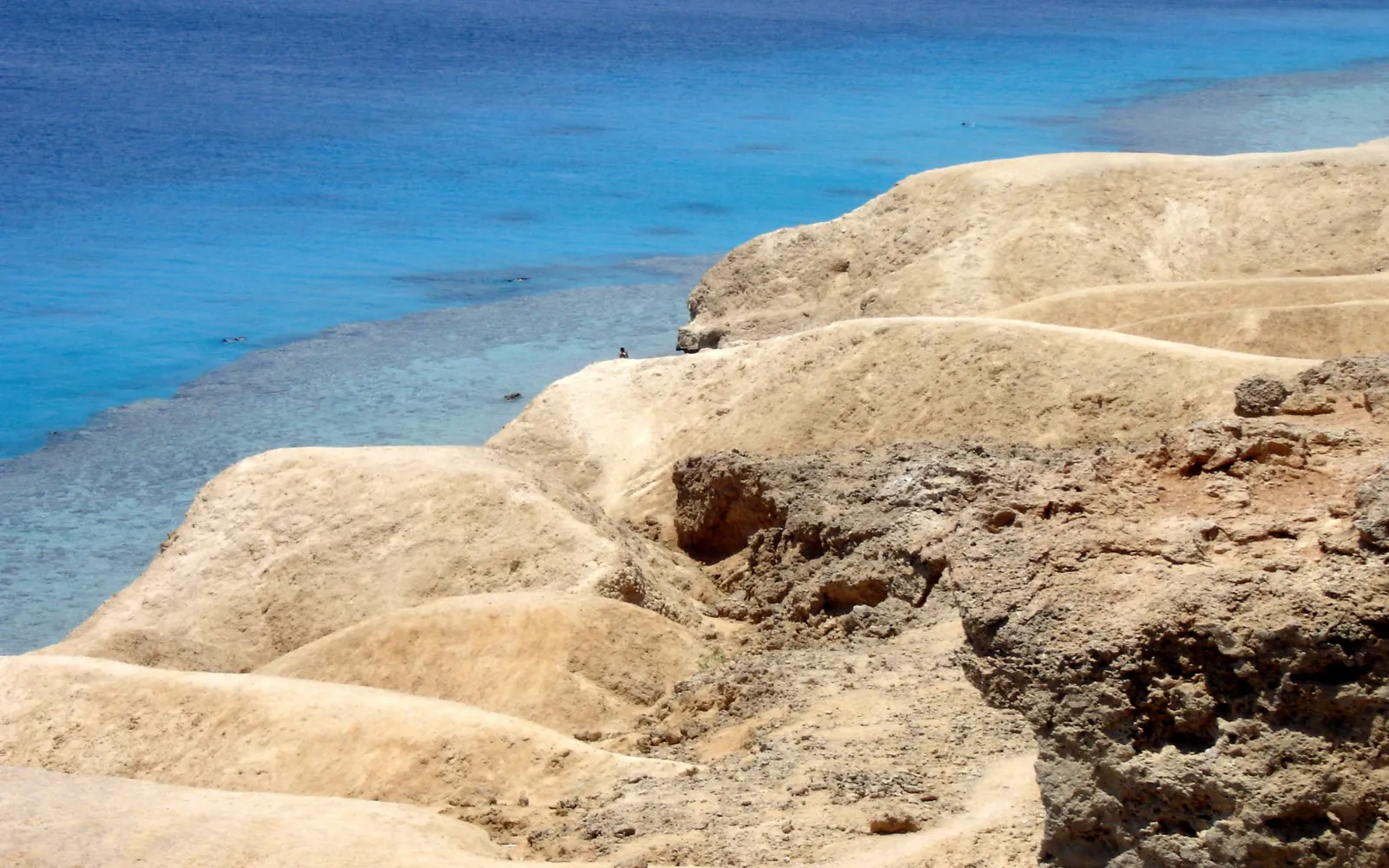 Sandy cliffs drop down to a clear turquoise ocean with a visible coral reef.