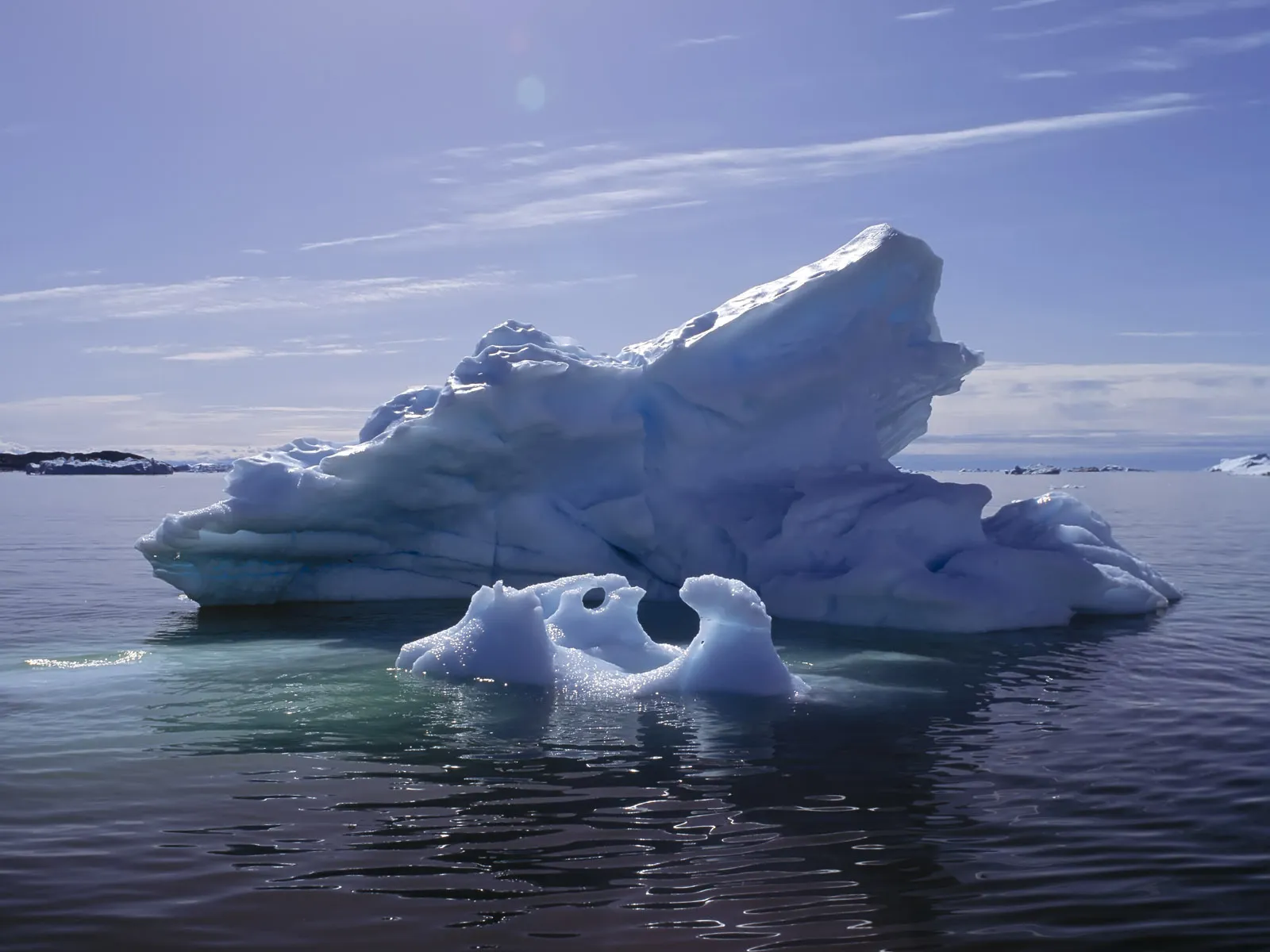 A large, intricately shaped iceberg floats in the bright sunlight of the Arctic Ocean.