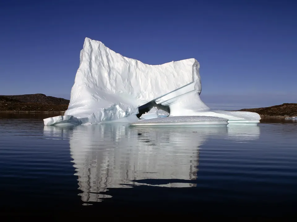 A natural iceberg formation floats serenely in dark blue water, reflecting the clear sky.