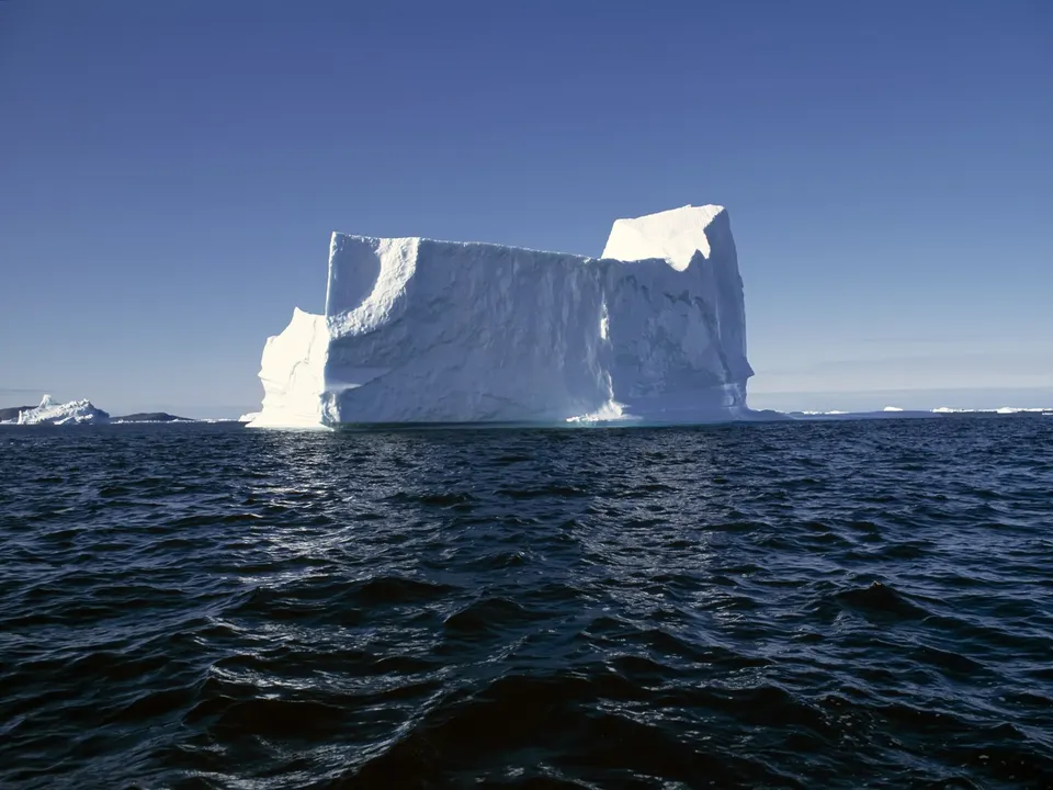 A colossal iceberg with a sculpted white surface floats in a deep blue, rippling ocean.