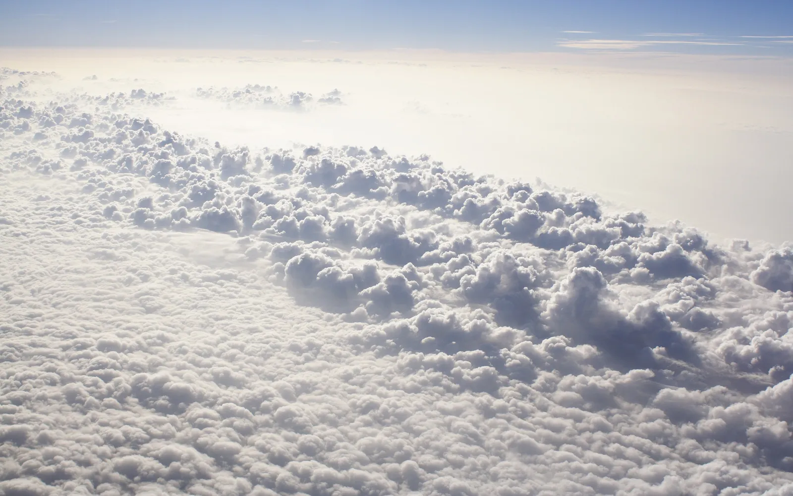 An aerial view of a vast expanse of fluffy white clouds under a pale blue sky.