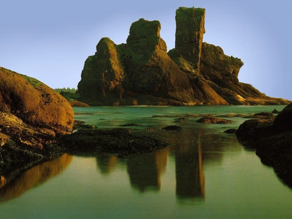 Large, rugged sea stacks rise from the water, with their reflections visible in the calm sea below.