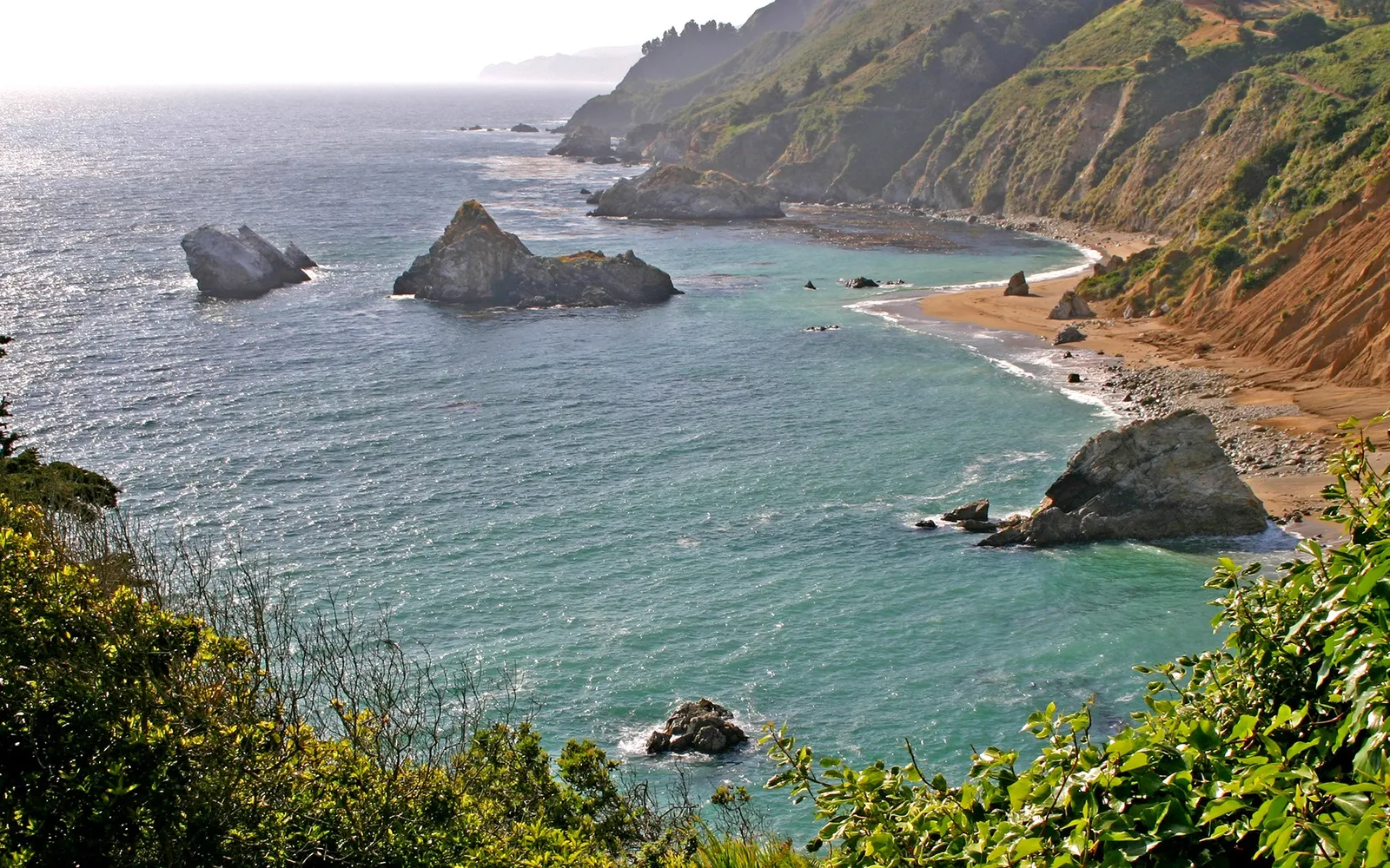 A dramatic coastline with steep, vegetated cliffs and rock formations in the turquoise ocean.