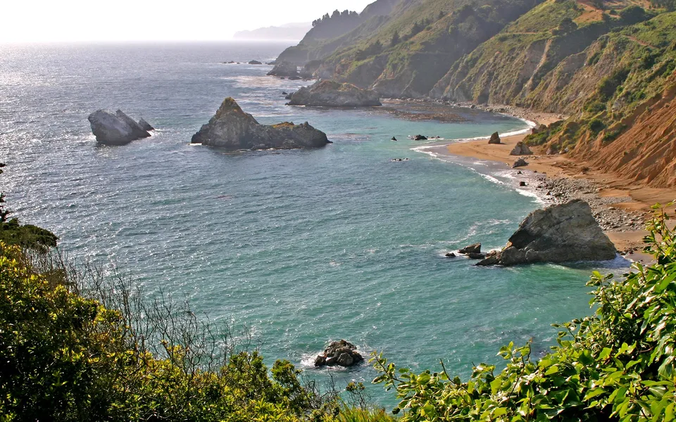 A dramatic coastline with steep, vegetated cliffs and rock formations in the turquoise ocean.